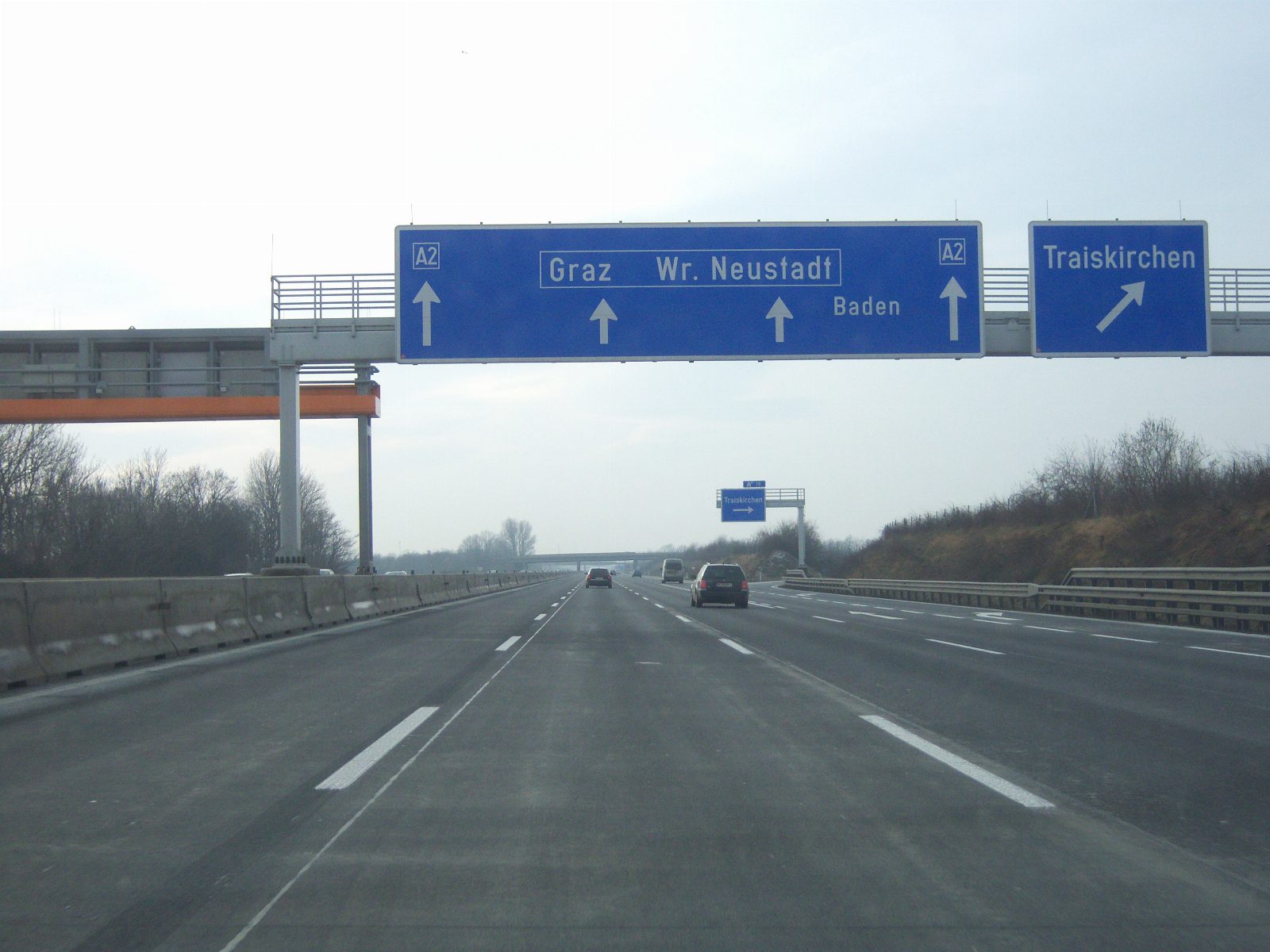 Autobahn mit blauen Wegweisern auf einer Schilderbrücke: geradeaus Graz, Wiener Neustadt und Baden, rechts die Ausfahrt Traiskirchen
