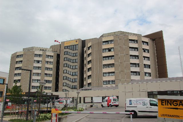 Mehrstöckiges, abgerundetes Spitalsgebäude mit Schriftzug Landesklinikum Baden, davor ein Rettungswagen und eine Schranke